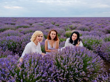 Farklı saç üç genç kız beyaz elbiseler içinde birlikte poz lavanta alanında renk.