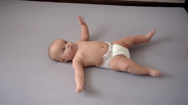 Schattige baby ligt op zijn rug en beweegt zijn armen en benen. Zijaanzicht. — Stockvideo