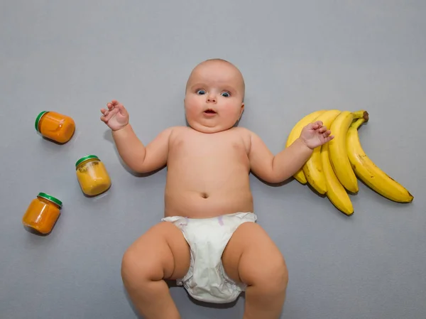 Förvånad Bebis Grå Bakgrund Med Bananer Och Burkar Barnmat — Stockfoto