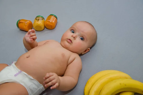 Baby Auf Grauem Hintergrund Mit Bananen Und Gläschen Babynahrung — Stockfoto