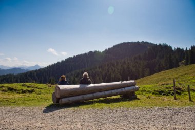 İki kişi kütük bir bankta oturmuş dağlara bakıyor..