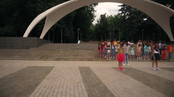 Vinnytsia Ukraina - 07 juni 2019: En grupp barn står och förbereder sig för att sjunga och dansa mot bakgrund av ingången till parken. Flygbild. — Stockvideo