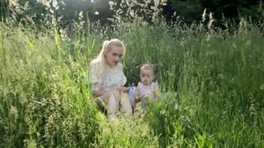 Küçük kızı olan genç bir kız çimlerin arasında oynuyor..