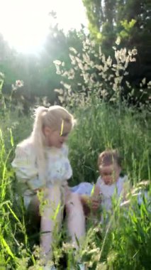 Küçük kızı olan genç bir kız çimlerin arasında oynuyor. Dikey video.