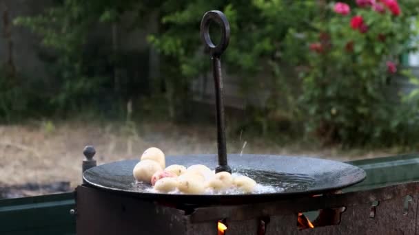 Jonge hele aardappelen gebakken in kokende olie tot een grote koekenpan boven een open vuur. Langzame beweging. — Stockvideo