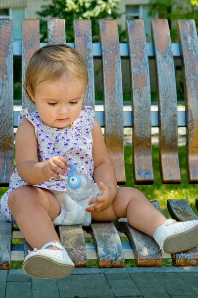 小さな女の子は公園のベンチに座って水を片手に — ストック写真