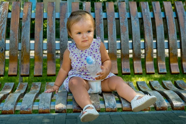 小さな女の子は公園のベンチに座って水を片手に — ストック写真