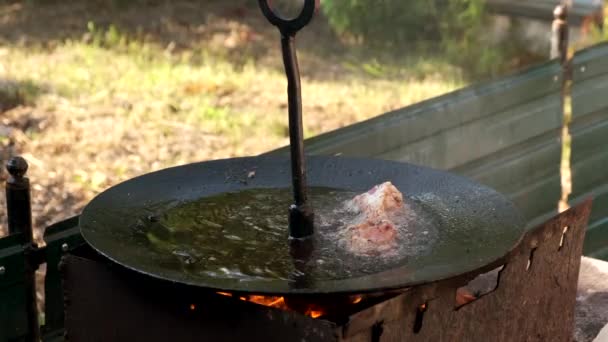 Una mano mette la carne in una grande padella sopra un fuoco aperto. — Video Stock