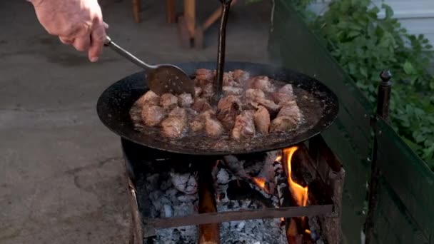 Vaření masa nad ohněm ve velké pánvi. Míchejte jídlo s velkou lžičkou. — Stock video