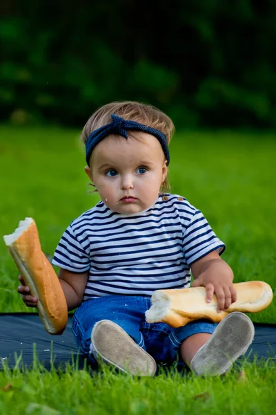 一个漂亮的小女孩坐在花园里的草坪上 手里拿着一个新鲜的面包 — 图库照片