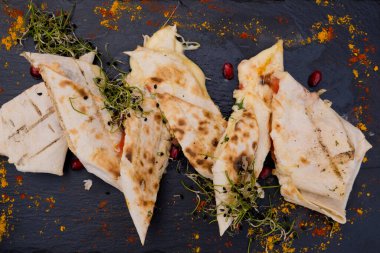Düz siyah tabakta peynirli lavaş. Mikro yeşil ve nar tohumlarıyla süslenmiş. Restoran yemeği..