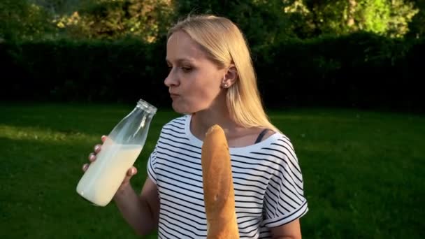 A young woman in jeans and a striped T-shirt drink milk from a glass bottle. — Stock Video