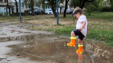 Turuncu çizmeli çocuk yağmurdan sonra su birikintilerinde yürür..