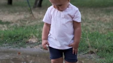 Turuncu çizmeli çocuk yağmurdan sonra su birikintilerinde yürüyor. Yakın çekim..