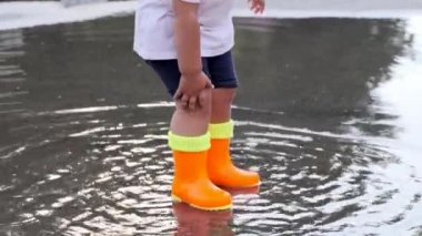 Turuncu çizmeli çocuk yağmurdan sonra su birikintilerinde yürüyor. Yakın çekim..