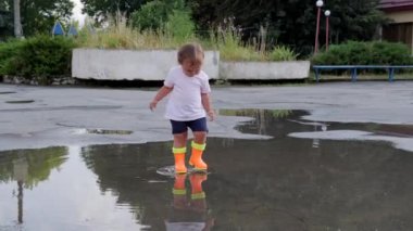 Turuncu çizmeli kız yağmurdan sonra su birikintilerinde yürür..
