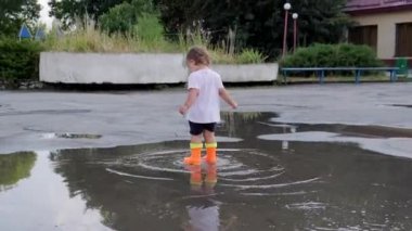Turuncu çizmeli çocuk yağmurdan sonra su birikintilerinde yürür..