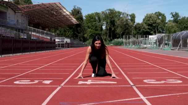 Femme en salopette noire se tient au début et commence à courir au stade public de la ville. Mouvement lent. — Video