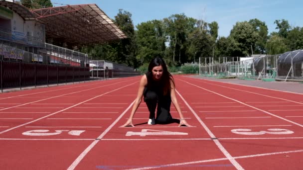 Vrouw in zwarte overall staat aan de start en begint te lopen in het openbaar stadion van de stad. Langzame beweging. — Stockvideo