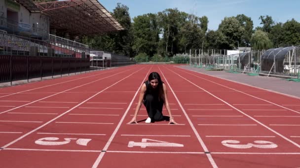 Nő fekete overálban áll az elején, és elkezd futni a városi stadionban. Lassú mozgás.. — Stock videók