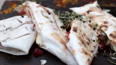 Düz siyah tabakta peynirli lavaş. Mikro yeşil ve nar tohumlarıyla süslenmiş. Restoran yemeği. Yumuşak odak.