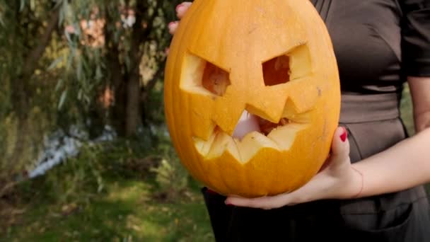 Mujer joven sosteniendo calabaza de halloween miedo en sus manos. Primer plano. Movimiento lento. — Vídeo de stock