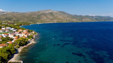 Arka planda bir kasaba olan güzel mavi bir okyanus. Su dalgalı ve evler beyaz.