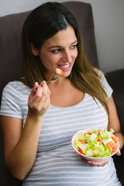 快乐的孕妇在家里吃一个健康的绿色沙拉与生菜 鳄梨和西红柿 — 图库照片