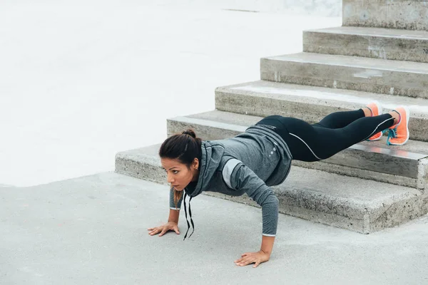 Strong fitness woman workout doing feet elevated push ups and exercising outdoor. Motivated female athlete training strength.