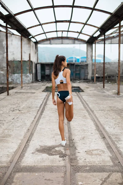 年轻适合女性跑步者伸展腿热身 然后再进行锻炼 在工业区旧城遗址锻炼的运动女孩 — 图库照片