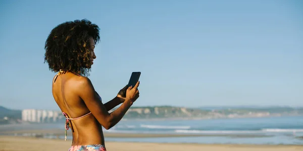 Jong afro haar vrouw met behulp van smartphone op het strand — Stockfoto