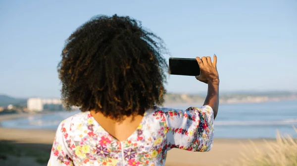 Afro kapsel jonge vrouw op het strand het nemen van foto — Stockfoto