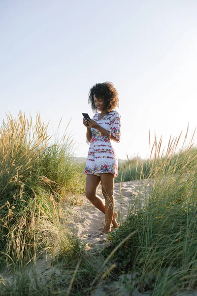 Kumsalda akıllı telefon kullanan genç afro saçlı kadın. — Stok fotoğraf