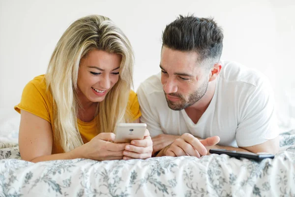 Joven pareja feliz usando teléfonos móviles en la cama en casa — Foto de Stock