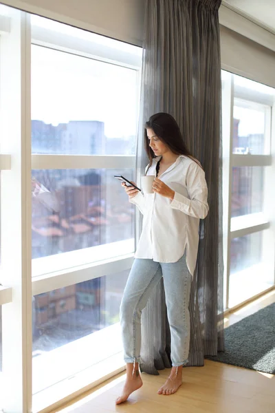 Mujer casual bebiendo café y mensajes de texto en el teléfono inteligente —  Fotos de Stock