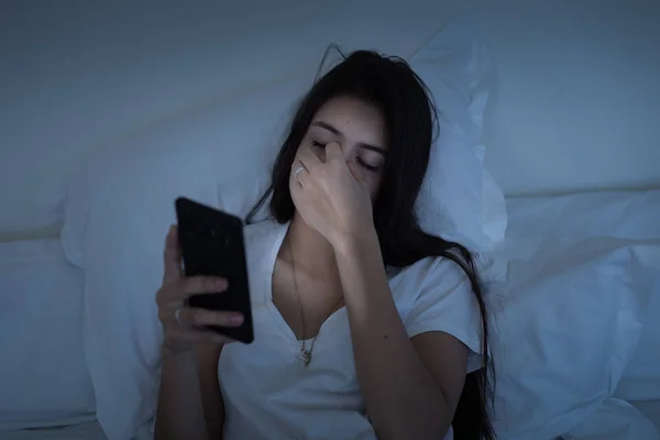 Sleepy girl with eye fatigue using smartphone in the bed