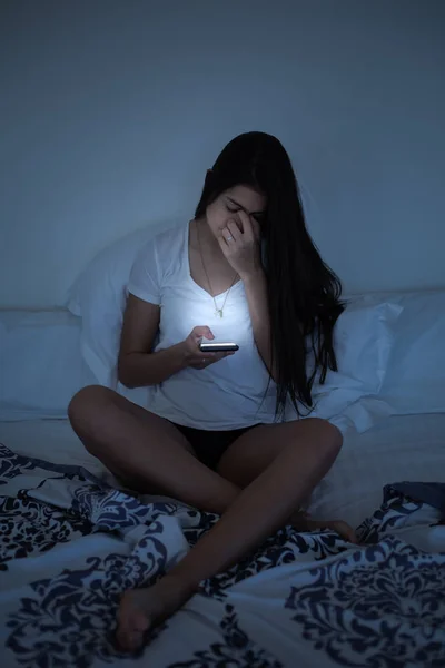 Chica somnolienta con fatiga ocular utilizando el teléfono inteligente en la cama —  Fotos de Stock