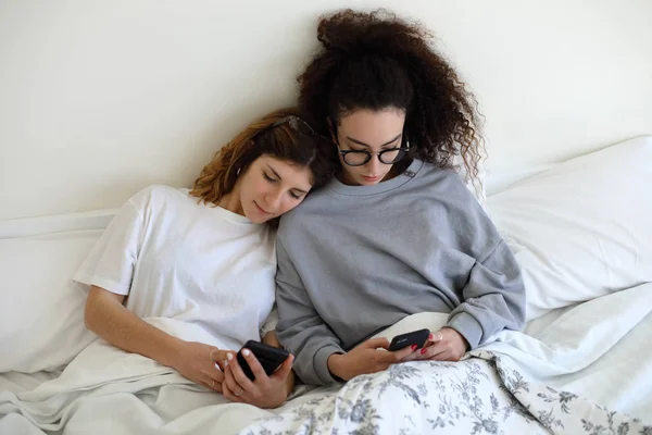 Duas mulheres na cama usando seus telefones celulares . — Fotografia de Stock