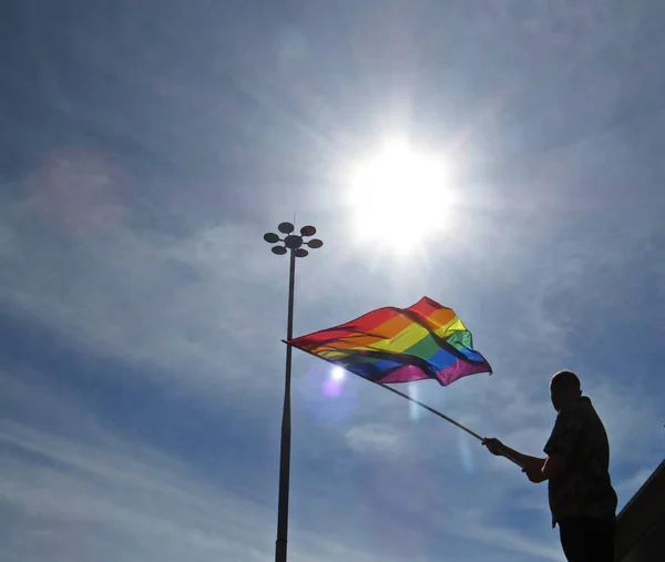 Geçit töreni sırasında arka planda bir lamba ve güneş ile gökkuşağı Lgbt bayrağı sallayarak adam