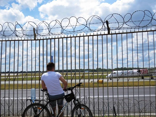 Adam çocuğu adam oturan çit dikenli tel ve havaalanında, Varşova, Polonya, Temmuz 2018 arıyorsunuz ile yanındaki bir bisiklet üzerinde