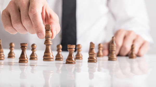 Бизнесмен, играющий в шахматы на белом столе, крупным планом показывает свою руку, перемещающую королевскую фигуру, концептуальный образ
.