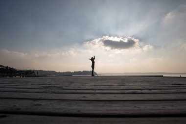 Gibi o ahşap güverte üzerinde duran bir kadın kolları olan yan düşük açılı görünüm karşı bulutlu gökyüzü outspread.