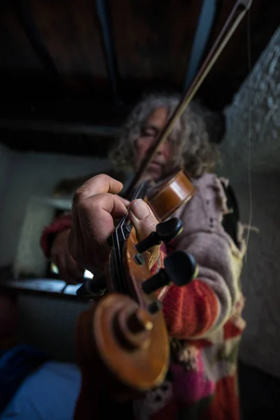 Old artist in old torn sweater full of holes with dirty nails enjoying his music as he plays a violin with focus to his fingers.