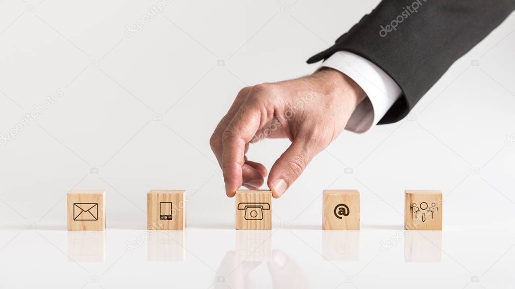 Cubes with contact symbols - envelope, at sign, telephone and human icon being placed on a white table by a businessman conceptual of communication and customer support.