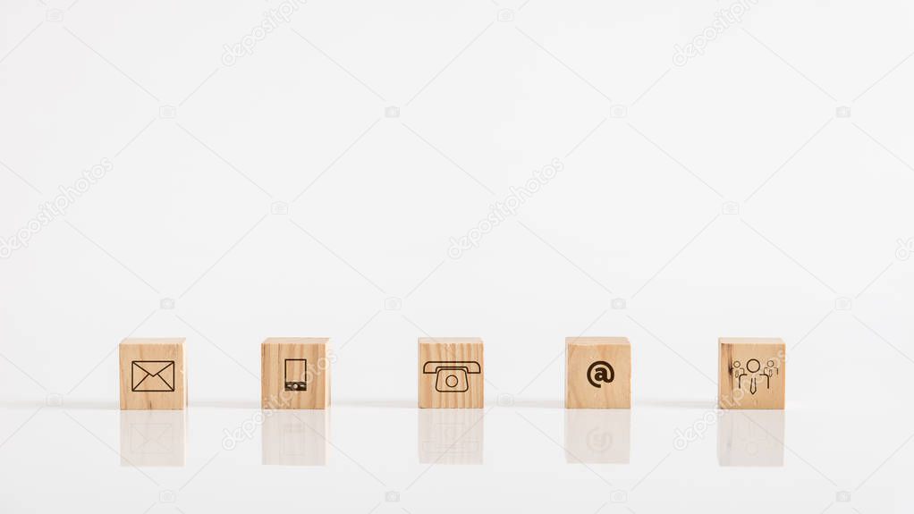 Online business communications concept of wooden cubes on white table displaying icons for email, a web address, mail, telephone and human icon.