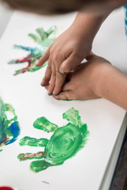 Yaratıcı çocuk yapım renkli palm basmak bir yaprak kağıda genel gider görünümünde elleri ile boyama.