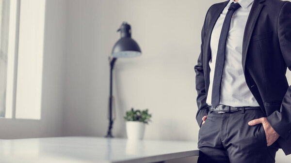 Retro effect faded and toned image of a businessman standing in office with his hands in the pockets of his suit pants.