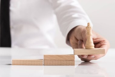 Ekip çalışması, başarı ve başarı bir kavram adımları bir dizi ilk olarak konumlandırılmış bir ahşap blok üzerinde bir Kraliçe satranç parça tutan işadamı.