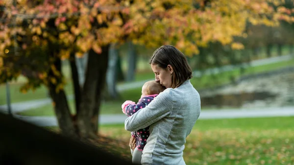 専用の若い母親は キスをし 穏やかな秋の日に公園で屋外彼女かわいい小さな女の赤ちゃんを保持 — ストック写真