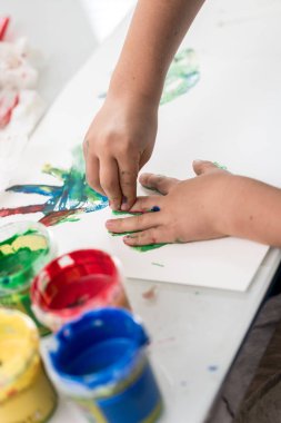 Genç çocuk parmak sanat dekore edilmiş onun palm görünümü kadar yakın desende aktarmak için bir yaprak kağıda basarak renkli boya ile yapıyor.